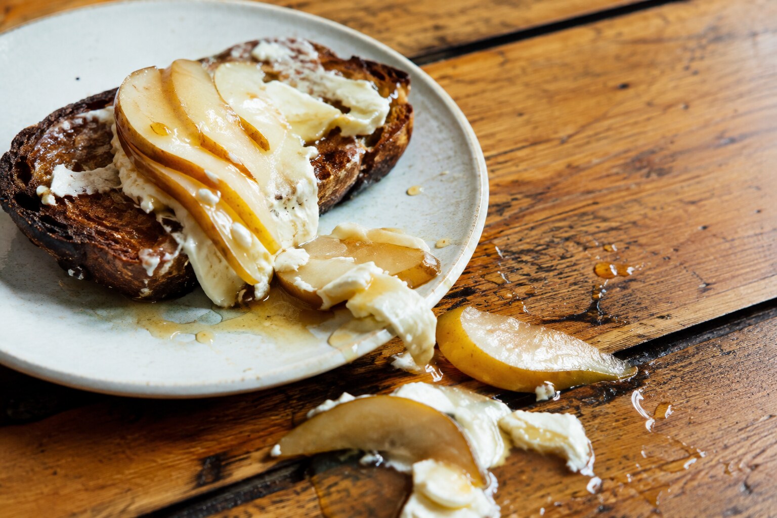 Pear toast toppled sideways with honey spilled on the table