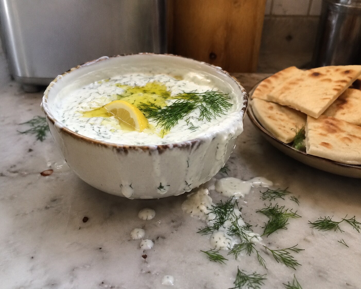 Yogurt dip splashed over its bowl with dill scattered nearby