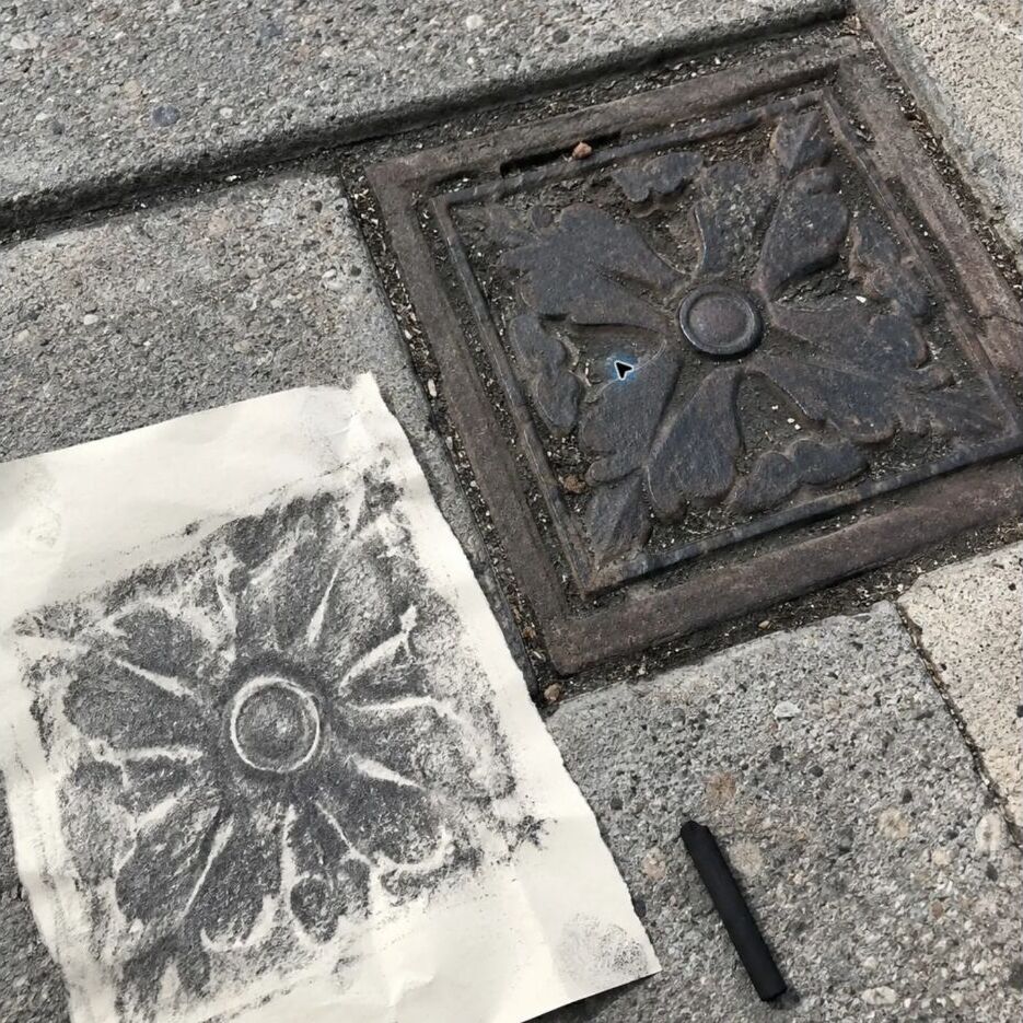 A sidewalk rubbing beside a patterned metal utility cover