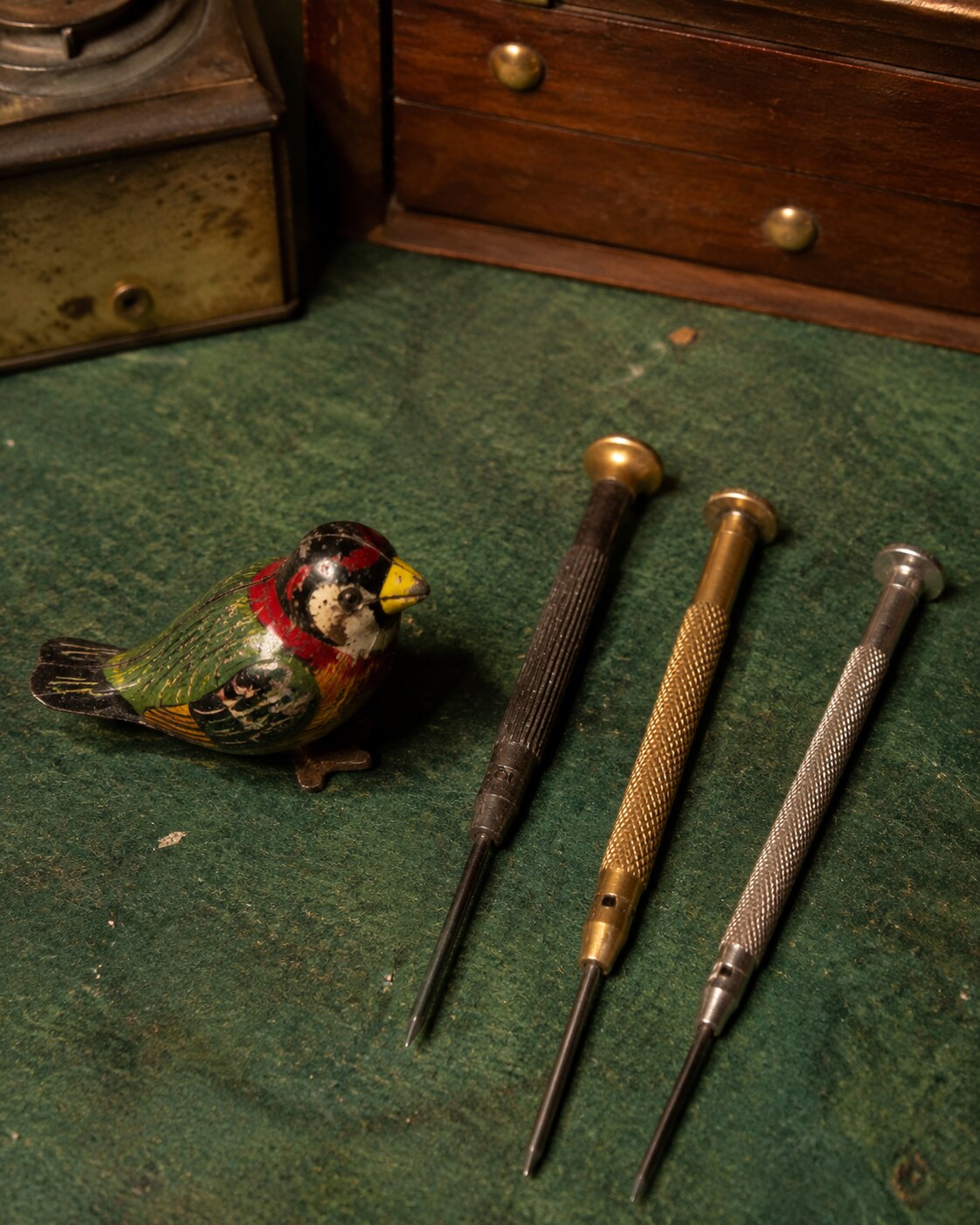 A painted tin bird beside tiny repair tools
